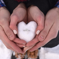 couples hand shaped like hearts holding engagement ring in snow heart