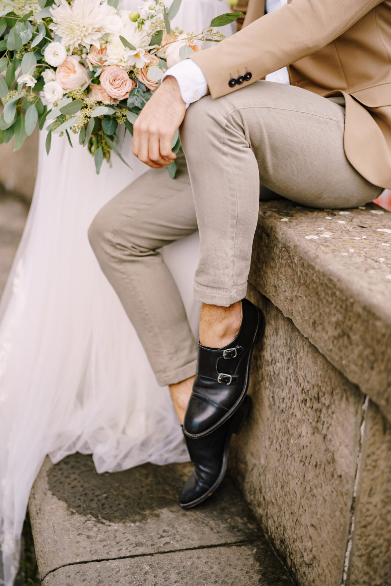 Close-up of the legs of the groom in light short pants and black leather shoes, the bride in a white dress with a bouquet in her hand