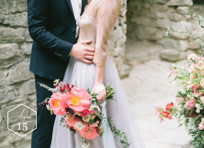 bride in blue wedding dress with pink flowers being embraced by groom next to a castle