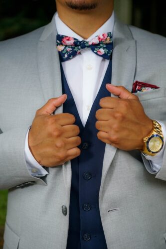 African American groom in grey suit with navy vest and floral bow tie holding lapels