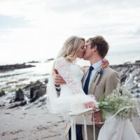 Groom holding bride while kissing her on the beach in Devon England