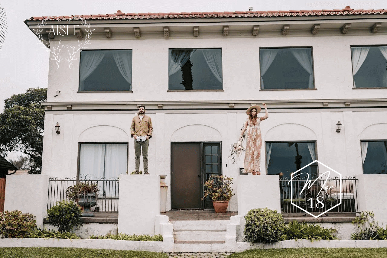 Boho bride and groom pose for portrait standing on pillars in front of Tuscany wedding venue - for wedding directory